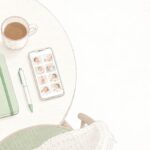 テーブルに置かれた育児日記のノートとペン、赤ちゃんの写真が並んだスマートフォンの画面